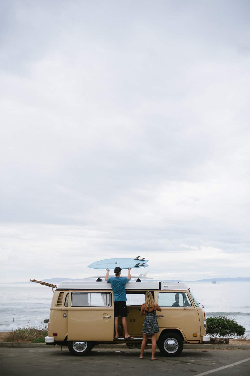 vw bus road trip surfer getting surfboard from top of van