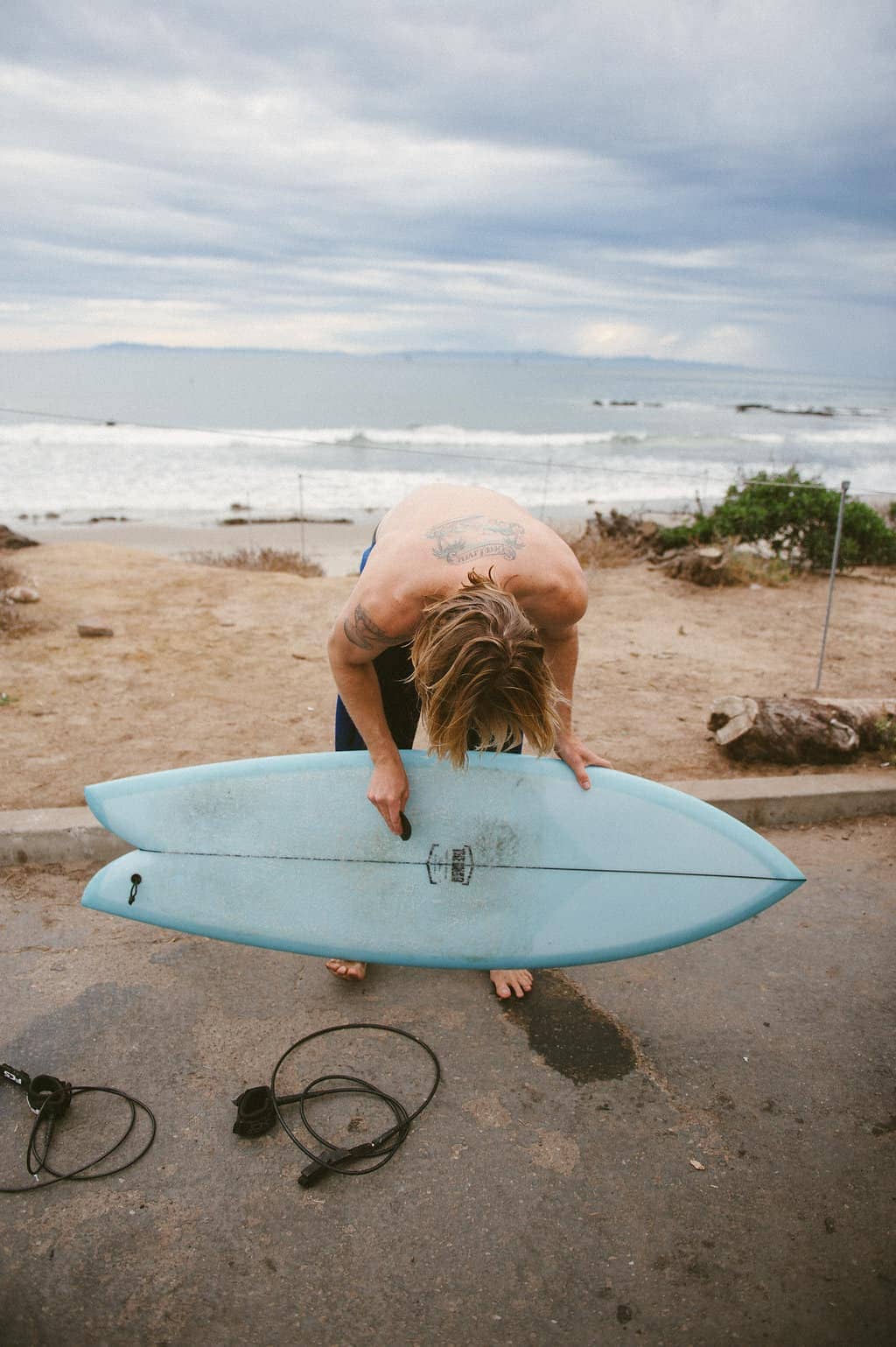 vw bus road trip surfer in wetsuit waxing blue surfboard