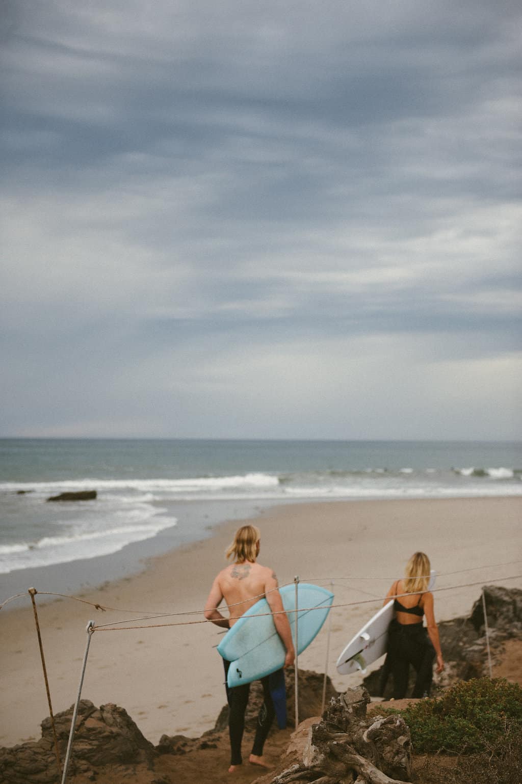 guy and girl surfers walking out to surf in wetsuits