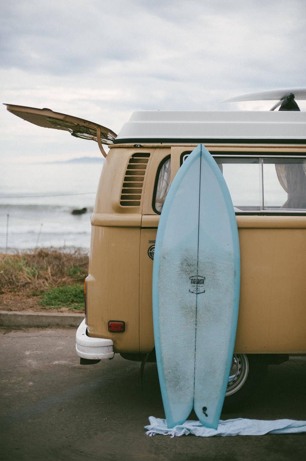 vw bus road trip blue surfboard leaning against yellow vw bus