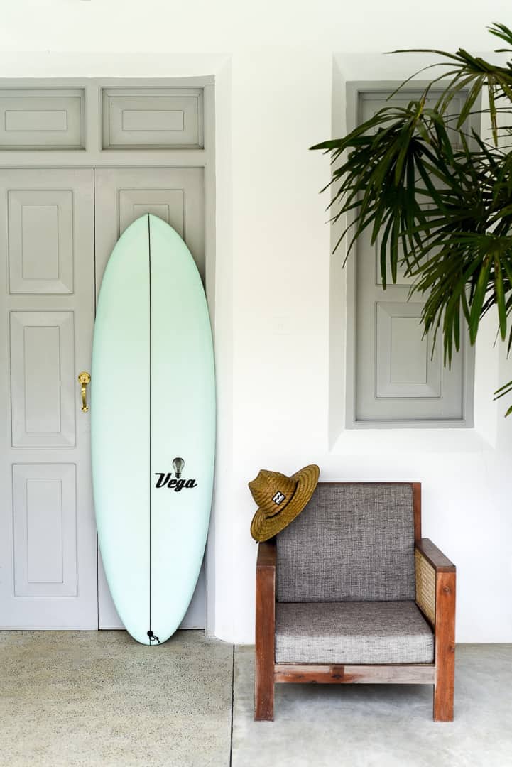 surfboard in front of boutique hotel room with straw hat hanging on chair