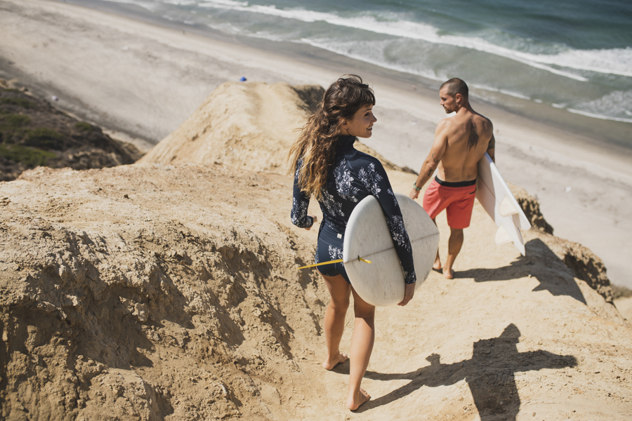 man and woman walking with surfboards wearing Vuori clothing