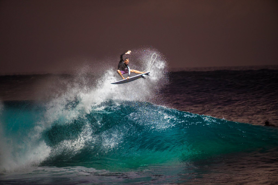 Surfer performing air maneuver on large wave at night - by Volcom surf brand