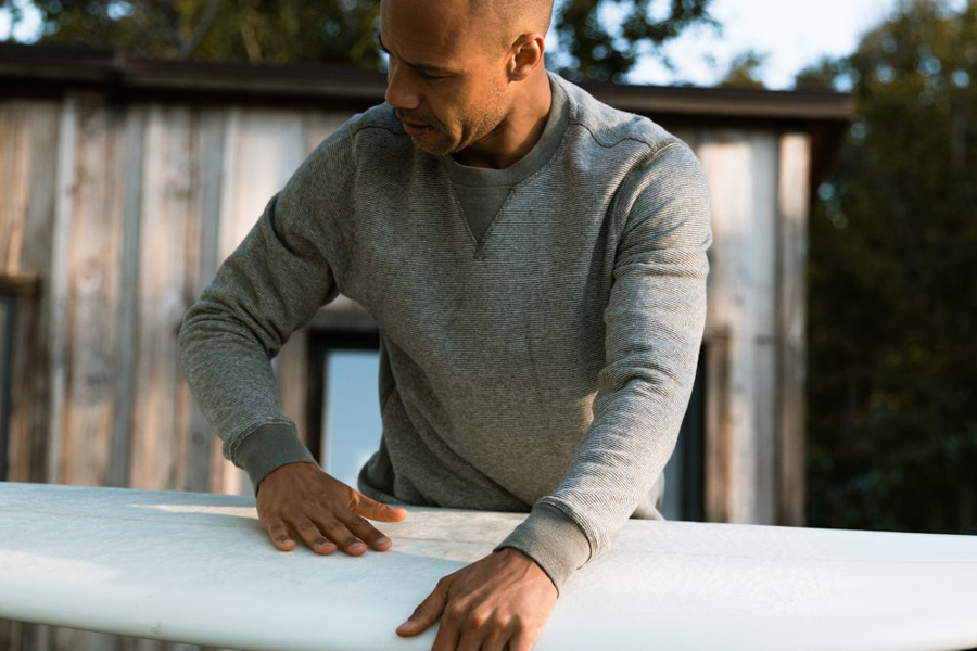 man holding surfboard wearing sweater by wellen surf company