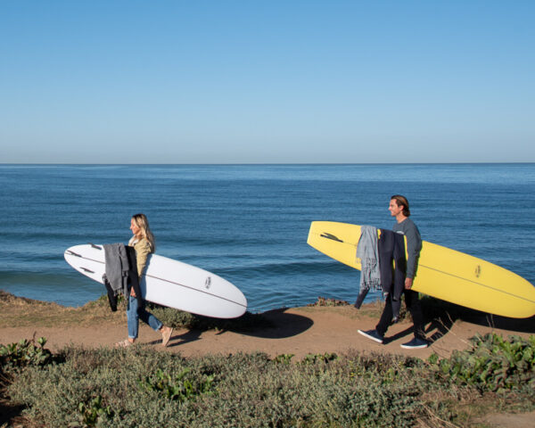 two beginner surfers with surfboards walking along the ocean to go surfing