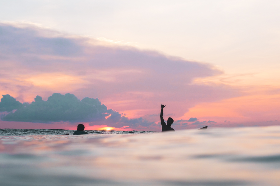 Surfista fazendo o sinal de shaka no oceano ao pôr do sol