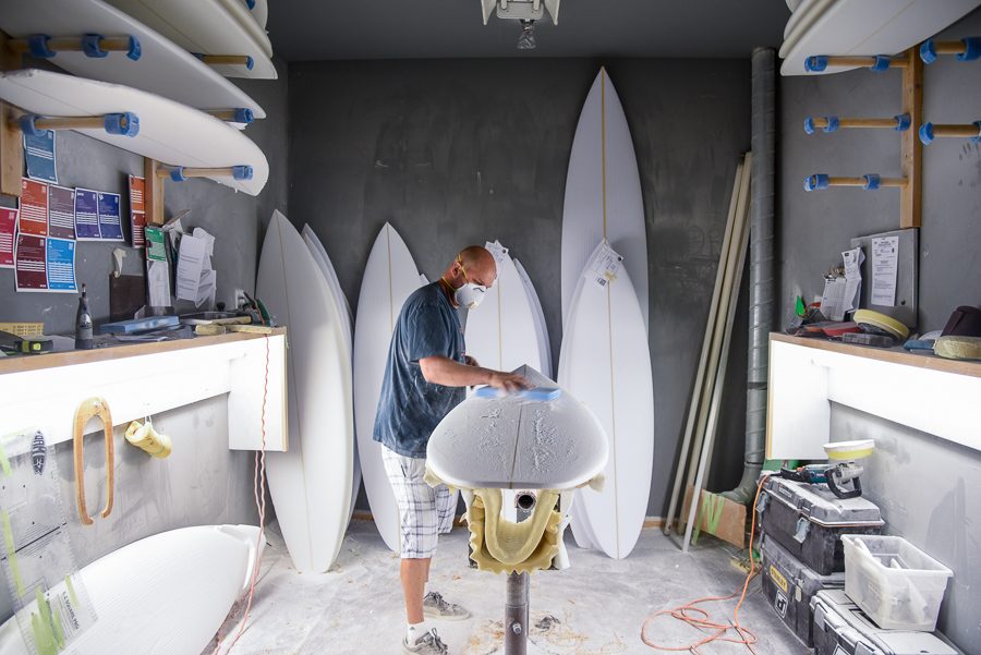 Um shaper de pranchas de surfe em uma baia de moldagem moldando uma prancha de surfe