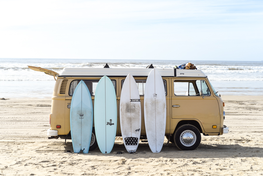 Surfboards of different sizes lined up on a VW bus on the beach