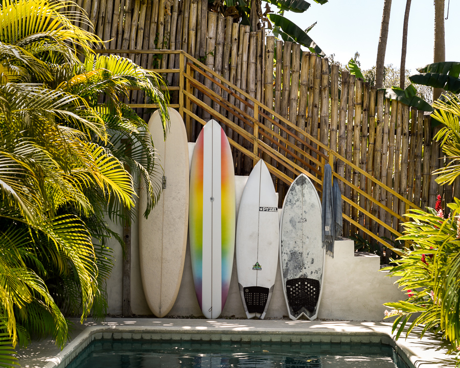 Four colorful surfboards of multiple different sizes lined up at the side of a pool