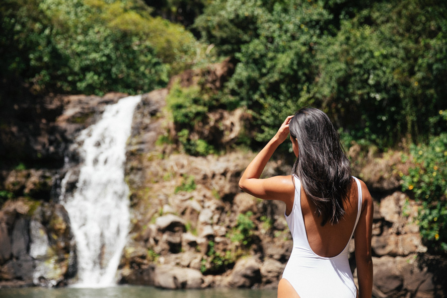 Woman standing at waterfall in white bathing suit